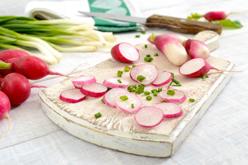 Sliced fresh red radishes and green young onions on white wooden background.  Healthy diet with radish. Ingredients for a light spring vegetable salad. Close up