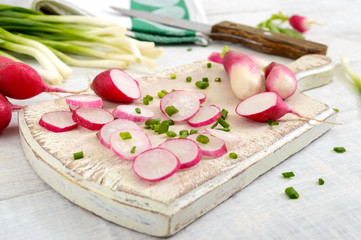 Sliced fresh red radishes and green young onions on white wooden background.  Healthy diet with radish. Ingredients for a light spring vegetable salad. Close up
