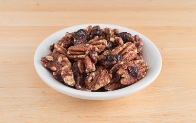 Sugar glazed pecans with dried cranberries in a white bowl atop a wood table.