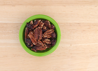 Top view of sugar glazed pecans with dried cranberries in a green bowl atop a wood table.
