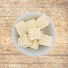 Several chunks of feta cheese in a bowl atop an old wood cutting board.