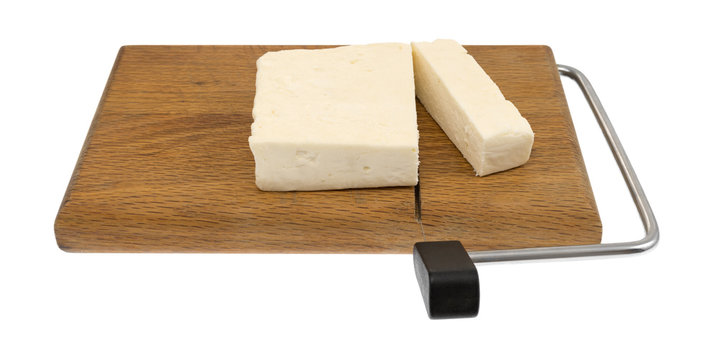 Chunks of feta cheese on a wood cheese slicer isolated on a white background.