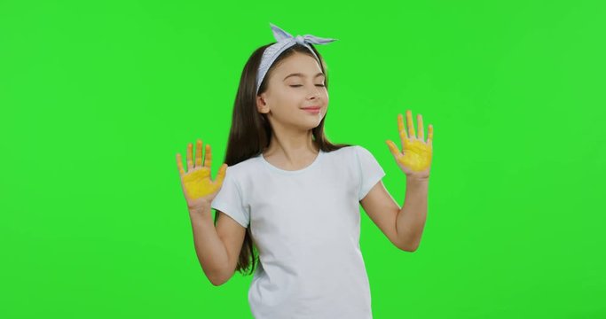 Pretty teen girl in the white T-shirt and with long hair posing to the camera with palms of the hands in yellow paint. Green screen. Chroma key.