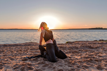 Fototapeta na wymiar stylish girl dancer kneeling in a fit of emotion on a sandy beach in the rays and glare of the sun at sunrise
