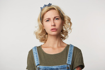 Indoor shot of cute blonde girl feels sad and tired, abused by someone, unhappy and mad. Isolated over white studio wall