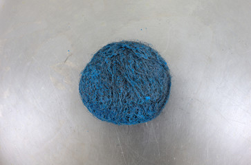 Top close view of a blue scouring pad on a stainless steel pan surface.
