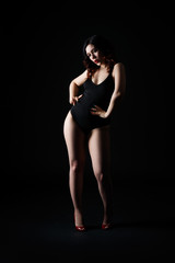 Fototapeta premium Beautiful sexy woman in bodysuit posing on black background, low key studio shot
