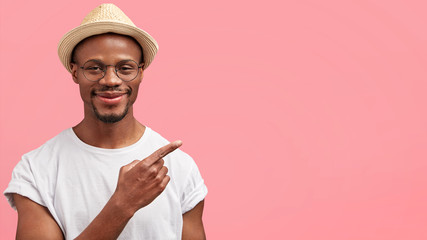 Check this out. Horizontal shot of positive funny African American male in straw hat points with...