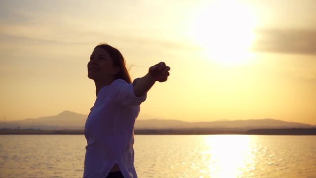 Dark silhouette of young woman spining at sunset on lake. Carefree female figure dancing at golden hour in slow motion