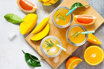 Fresh refreshing summer drinks. Multifruit drinks of citrus and mango with ice, smoothies on a light stone or slate background. Copy space, top view flat lay background.