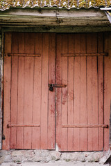 Old wooden door closed on the lock. Peeling paint. House. Barn. Doors red. The door to the hinges.
