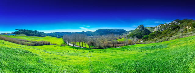 Beautiful panoramic pastoral, surrounded by evergreen trees on steep hills. Farm fields of red soil in the valley of the Alcabrichel river. A typical agricultural landscape near Vimeiro in Portugal.