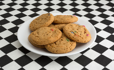 Several candy cookies on a white plate atop a checkerboard tablecloth.