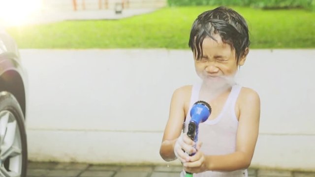 Slow motion of joyful little boy playing water with a water hose and spray water to his face at home