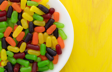 Top view of chewy colorful candy on a white plate atop a yellow painted wood table top.