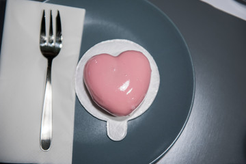 Light pink, heart shaped cake served on the gray plate with fork