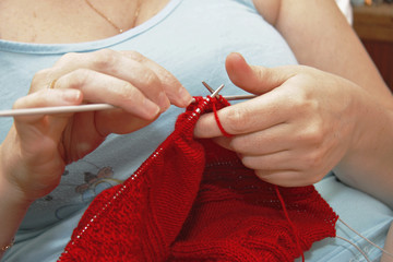 Obraz na płótnie Canvas Woman knits with knitting needles red sweater from natural woolen threads