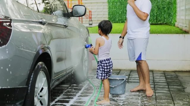 Slow motion of happy little boy and his father using a water hose to wash a car
