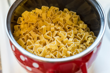 Heart shaped pasta in red pot with white dots on stove. Concept: preparing meal with love
