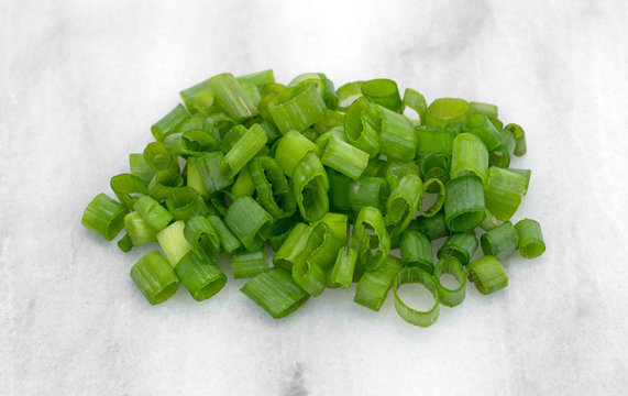 A small portion of chopped green onions on a marble cutting board.