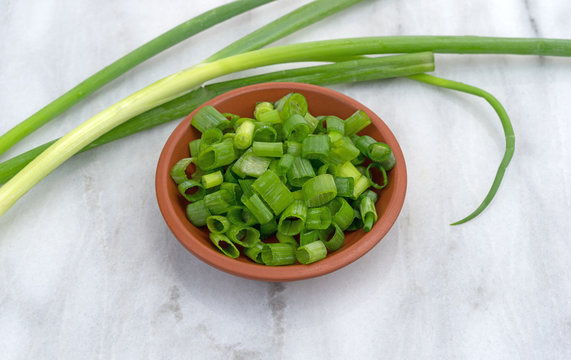 Chopped green onions in a small red clay bowl atop a marble cutting board.