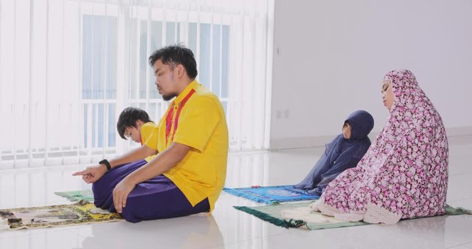 Asian muslim family praying together while wearing islamic clothes at home. Shot in 4k resolution