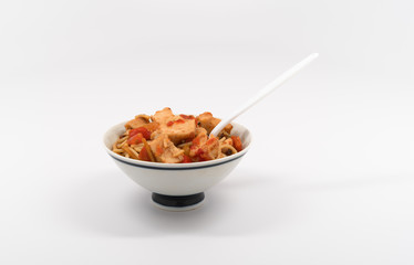 Bowl of chicken breast pieces in angel hair pasta on a white table top.