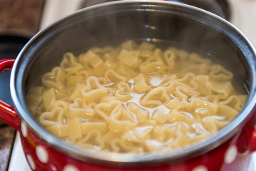 Heart shaped pasta in red pot with white dots on stove. Concept: preparing meal with love
