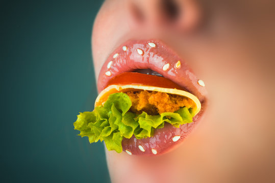 Fast Food For Business Lady. Female Face And Burger Inside. Close Up Pink Woman Lips With Tomato, Cheese, Chop And Lettuce Inside. Seductive Female Lips With Sesame Full Of Salad. Delicious Mouth