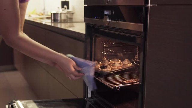 Woman's hand opens oven, takes burnt cookies, smoke from overcooked food coming