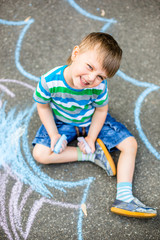 Naklejka premium Cute boy and girl drawing with chalk on the sidewalk in the park.