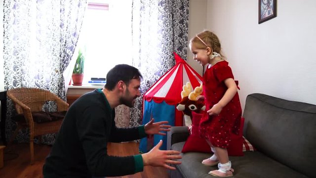 A cute little baby jumps from the sofa into her father's hands in slow motion.