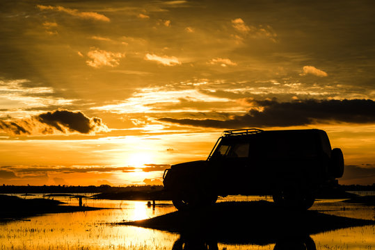 Silhouette car off road on the river over sunset background.