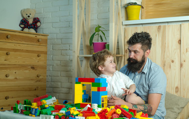 Cute boy looks at father. Handsome father and his cute son looking at each other and smiling while spending time together at home. Family and toys, happy beautiful child and bearded stylish father