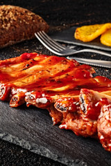 Closeup of baked pork ribs with barbecue sauce on slate bottom, with baked potatoes and spices, bread and cutlery. Front view