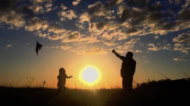 Silhouette of a happy family playing a kite. Grandpa and little girl are playing at sunset with a kite.