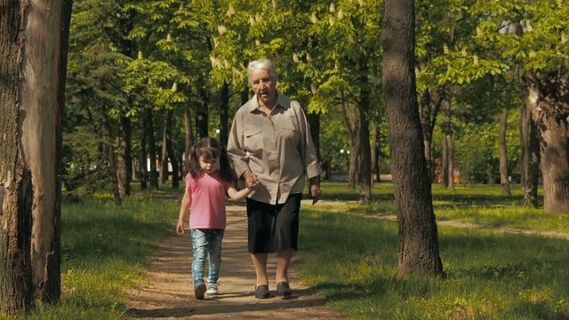 An elderly woman with a child is walking in the park. Grandmother with granddaughter on a walk in the park.