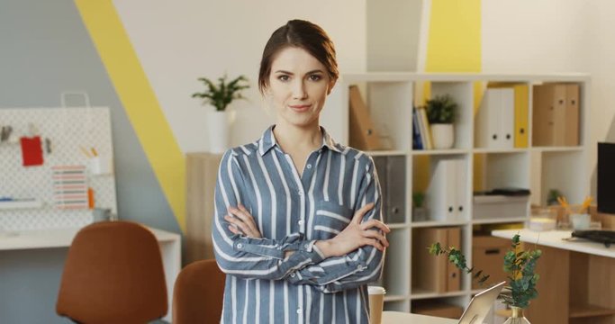 Portrait shot of the young Caucasian attractive woman with hands crossed in front standing and posing in the urban office. Inside