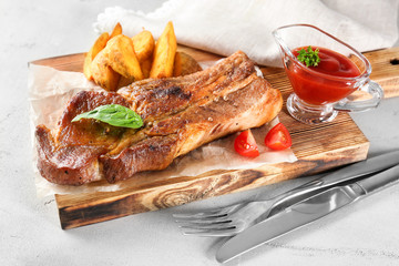 Wooden board with delicious grilled rib, vegetables and tomato sauce on table