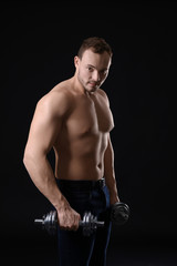 Fototapeta na wymiar Muscular young bodybuilder with dumb-bells on dark background