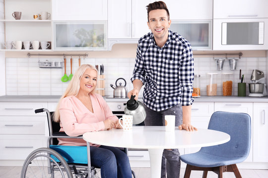 Young man taking care of mature woman in wheelchair indoors