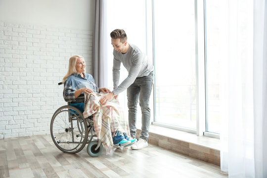 Young man taking care of mature woman in wheelchair indoors