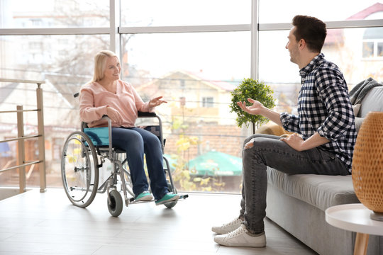 Young man talking to mature woman in wheelchair indoors