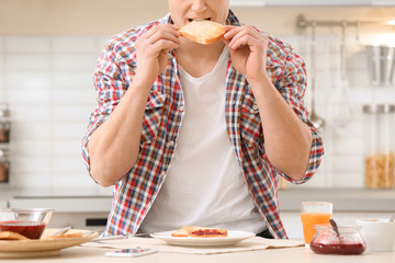 Young man eating tasty toasted bread at table in kitchen