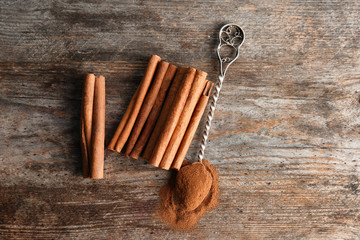 Spoon with aromatic cinnamon powder and sticks on wooden background