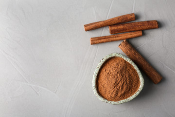 Bowl with aromatic cinnamon powder and sticks on grey background