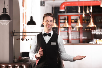 Waiter in elegant uniform with menu at workplace