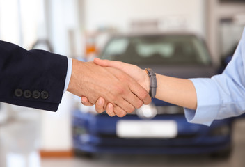 Young salesman shaking hands with client in car dealership