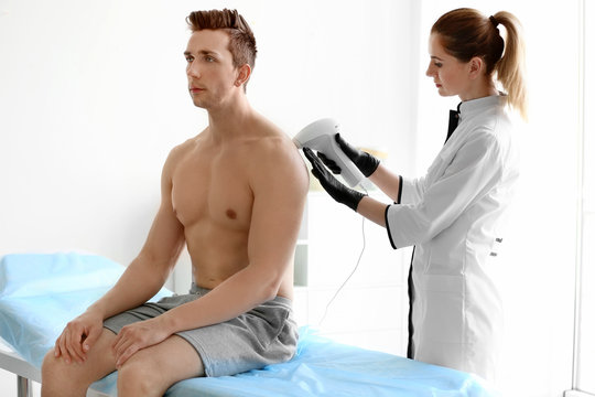 Man undergoing hair removal procedure with photo epilator in salon