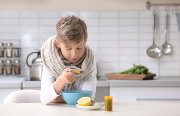 Sick little boy eating broth to cure cold at table in kitchen